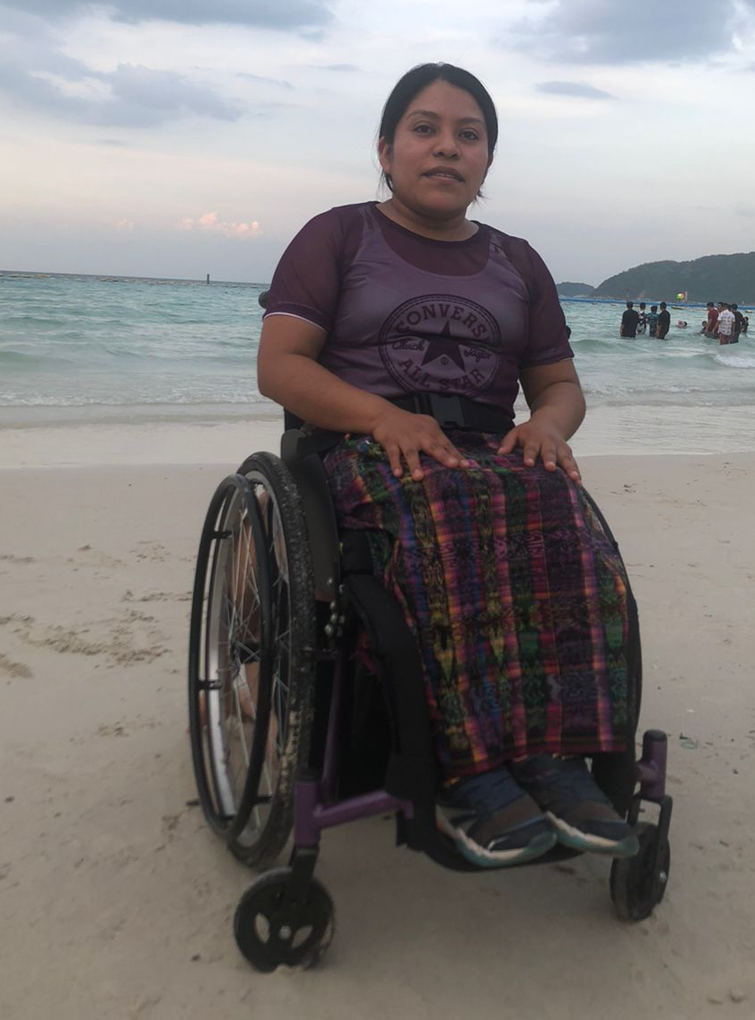 The image shows Floridalma Bocel Raxtún sitting in a wheelchair on a beach in Guatemala