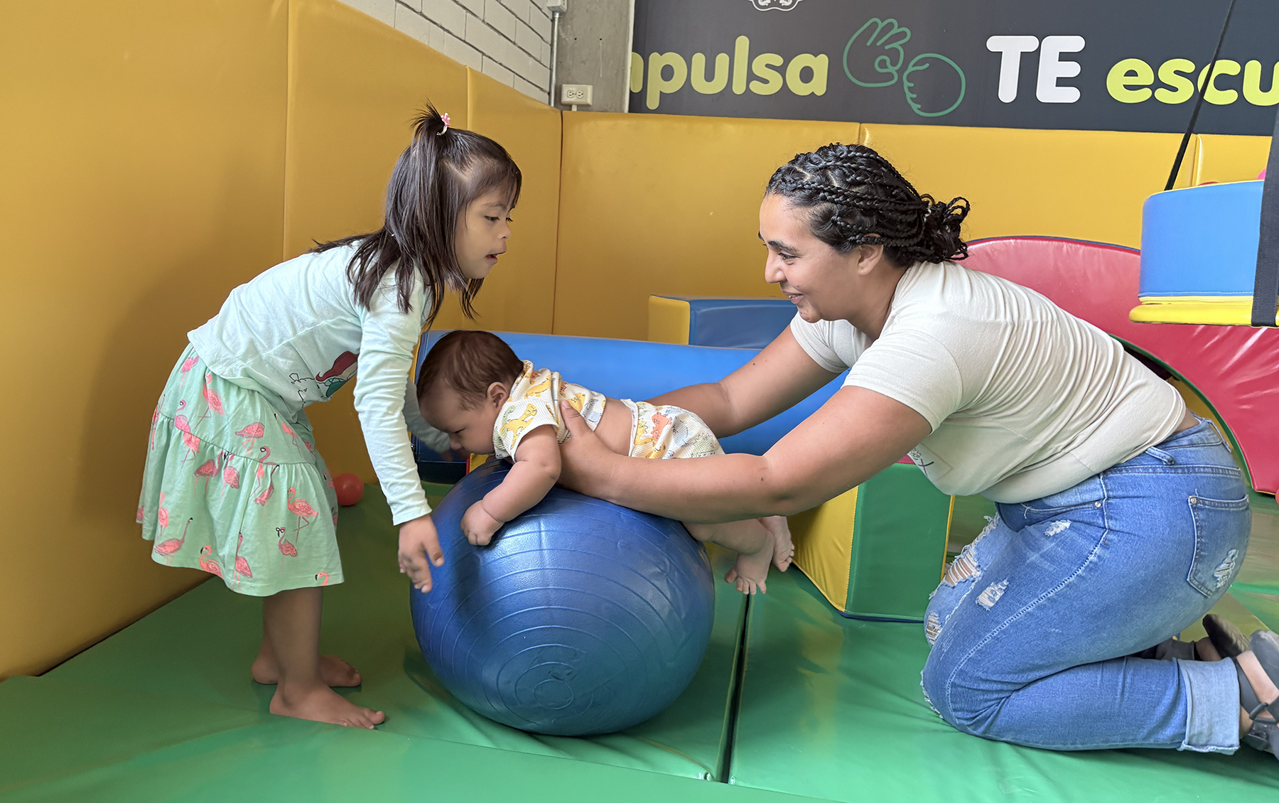 A woman and two children play with a pilates ball